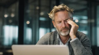 Professional sitting at a desk with eyes closed, rubbing their temple in quiet frustration with others